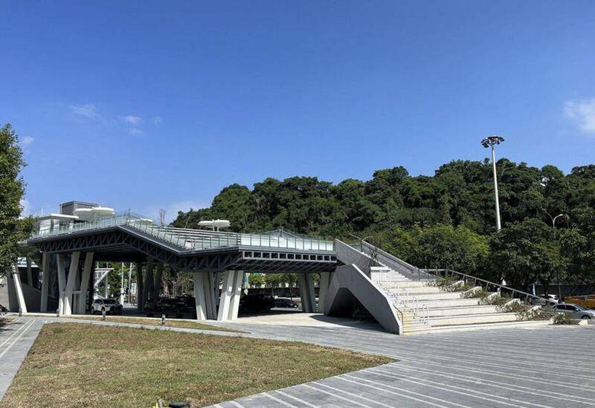南港立體連通大平臺遠攝全景：寬闊的鋼構平臺跨越道路，上方設有流線型頂篷與綠色植栽。