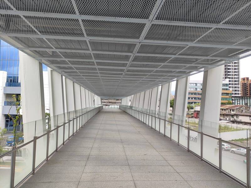 南向主橋通廊內部：走道地面平整且寬敞，兩側設有透明玻璃護欄與簡潔的鋼構支撐，視野開闊。